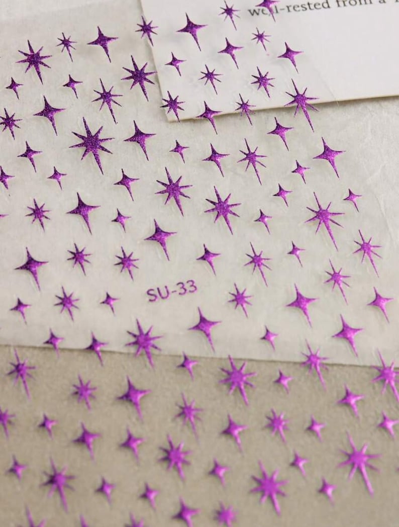 May include: A sheet of clear adhesive paper with a repeating pattern of purple glitter stars. The sheet is labeled "SU-33".