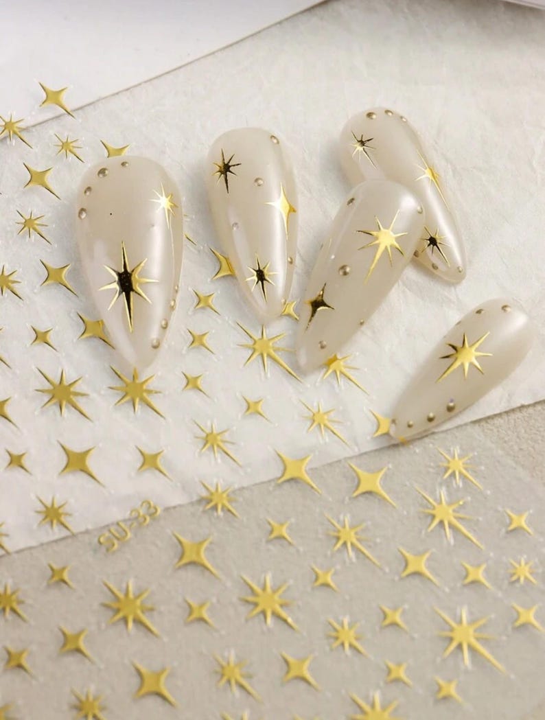 May include: Gold nail art stickers with a starburst design. The stickers are on a clear sheet with a white background. The sheet has the text "SU-233" printed on it.