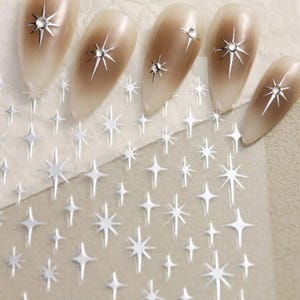 May include: Nail art stickers with a silver glitter star design. The sheet includes multiple stars of varying sizes. The sheet also has the text "SU-33" printed on it.