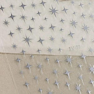 May include: A sheet of clear adhesive paper with a repeating pattern of silver star stickers. The sheet is labeled "SU-38".