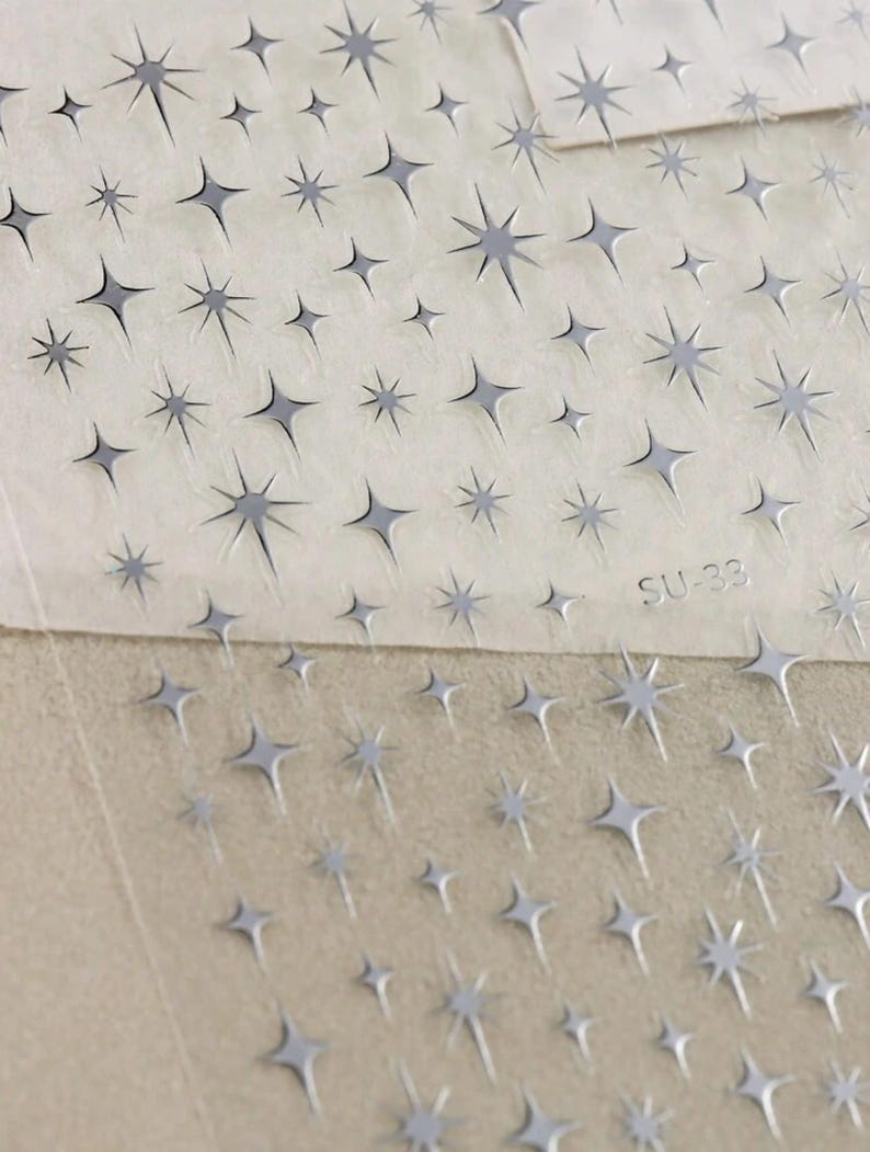 May include: A sheet of clear adhesive paper with a repeating pattern of silver star stickers. The sheet is labeled "SU-38".