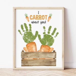 May include: Framed art print with the text "I CARROT about you!" featuring green handprints and orange carrots. The carrots are in a wooden crate, and the print has a light wood frame.