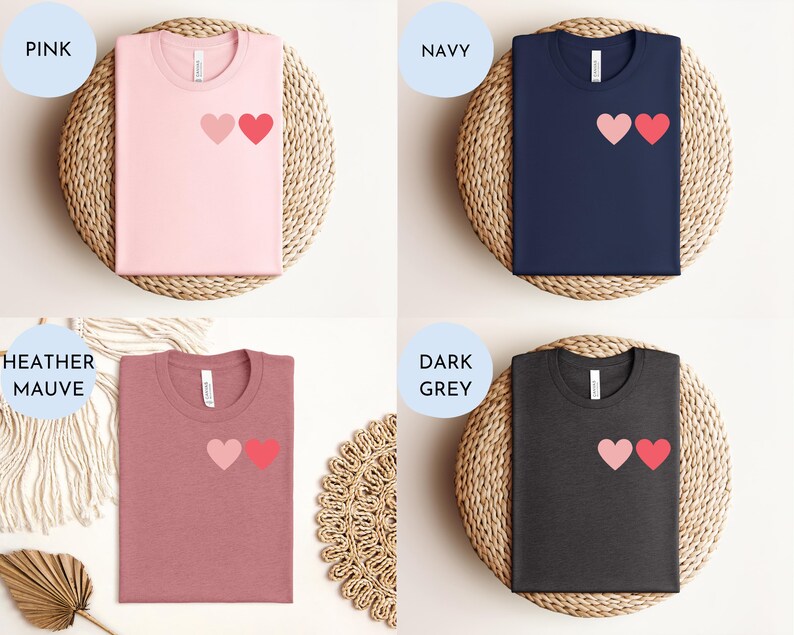 May include: Four t-shirts with a two-heart graphic design. The shirts are shown in pink, navy, heather mauve, and dark grey.