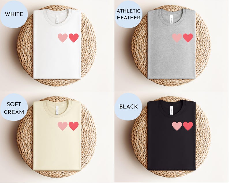 May include: Four t-shirts with a graphic of two pink hearts on the left chest. The t-shirts are displayed on a woven background. The t-shirt colors are white, athletic heather, soft cream, and black.