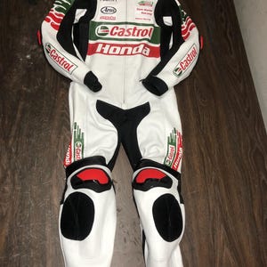 Könnte beinhalten: Weiß-schwarzer Rennanzug mit roten und grünen Akzenten. Der Anzug zeigt das "Castrol Honda" Logo und andere Sponsorenlogos. Knie- und Ellbogenschutz inklusive.