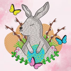 May include: A grey bunny rabbit with closed eyes sits on a blue and yellow patterned Easter egg. The bunny is surrounded by green leaves and white flowers. There are two butterflies, one yellow and one blue, in the background.