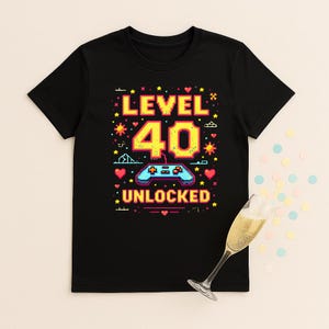 May include: Black t-shirt with a colourful graphic design. The design features the words "LEVEL 40 UNLOCKED" with a video game controller and stars. The number 40 is in a large, bold font.