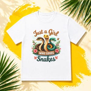May include: White t-shirt with a graphic of three snakes in brown, orange, and green, with the text "Just a Girl Who Loves Snakes." The design includes flowers and a butterfly, creating a vibrant look.
