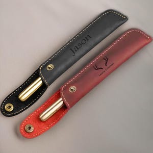 May include: Two personalized leather pen cases. One is black with the name "Jason" engraved on it. The other is red with a deer antler design and the name "Laurie Coleman" engraved on it.