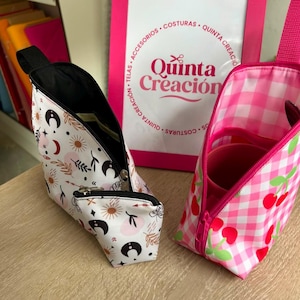 May include: Two zippered pouches with carrying straps. One pouch is white with a black and red celestial pattern of moons, suns, and leaves. The other pouch is pink and white gingham with a red cherry print and a pink interior lining.