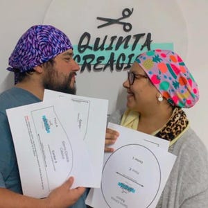 Puede incluir: Dos personas con gorros quirúrgicos estampados, uno morado y otro rosa con diseños de frutas, sosteniendo papeles con patrones. Los gorros son parte de un tema médico o de atención médica. El texto "QUINTA CREAGI" es visible en la pared.
