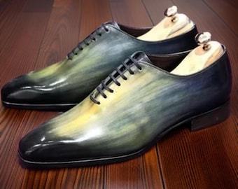 May include: A pair of black leather dress shoes with a green and yellow ombre effect. The shoes have a lace-up closure and a pointed toe.