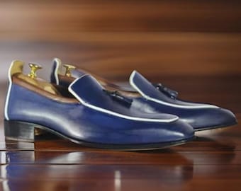 May include: A pair of blue leather tassel loafers with white trim. The loafers have a pointed toe and a low heel.