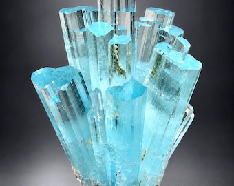 May include: A cluster of translucent, light blue aquamarine crystals featuring elongated, hexagonal prismatic structures with sharp, flat terminations. The mineral specimen displays vertical striations along the sides and internal inclusions.