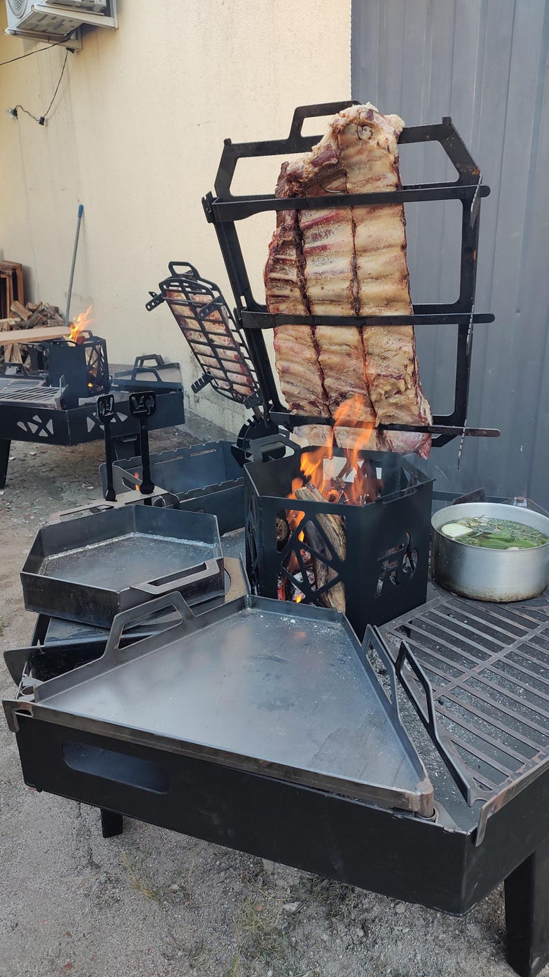 Puede incluir: Un sistema de parrilla exterior de metal negro con un soporte vertical que sostiene un costillar sobre fuego abierto, una plancha triangular plana, una caja de fuego hexagonal, una rejilla de cocci&oacute;n y una olla plateada con hierbas.