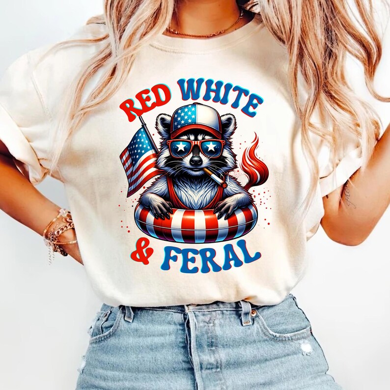 May include: Cream-coloured t-shirt with a raccoon wearing sunglasses, a hat, and a life preserver, holding an American flag and a cigarette. The text "RED WHITE & FERAL" is printed in red and blue.