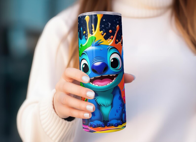 Puede incluir: Un vaso azul con un personaje de dibujos animados sonriendo ampliamente, sobre un dise&ntilde;o de salpicaduras colorido. El personaje es azul con la boca rosa. El fondo presenta salpicaduras verdes, naranjas y amarillas, creando un dise&ntilde;o vibrante.