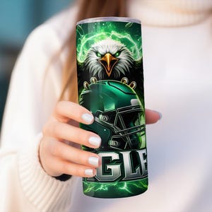 May include: Green and black stainless steel tumbler featuring a graphic of a bald eagle holding a football helmet. The text "EAGLES" is printed on the tumbler.
