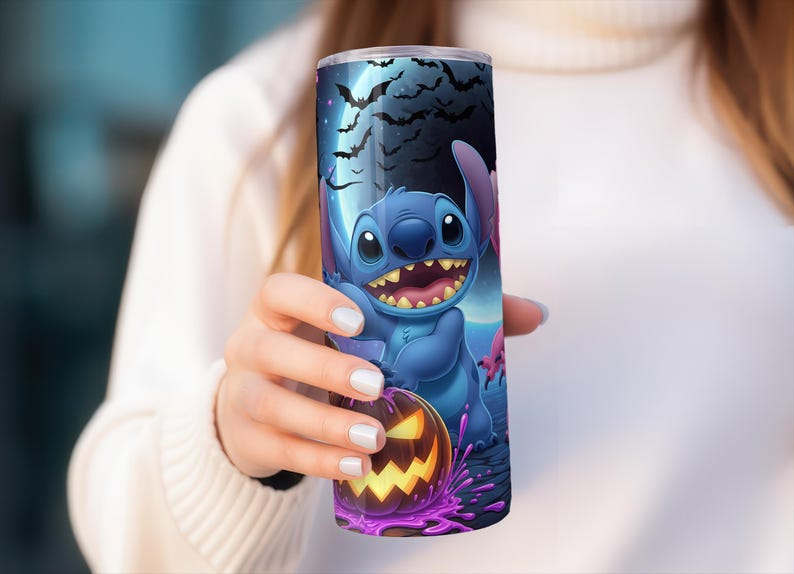 Pode incluir: Um copo azul com um design de Halloween com Stitch, uma ab&oacute;bora e morcegos contra um c&eacute;u iluminado pela lua. O copo &eacute; segurado por uma pessoa que usa um su&eacute;ter branco.