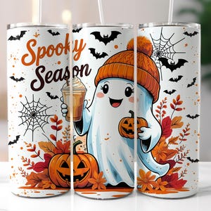 May include: White tumbler featuring a cartoon ghost holding a pumpkin and a coffee drink, wearing an orange beanie. The tumbler has the words "Spooky Season" and is decorated with bats, spiderwebs, and fall foliage.