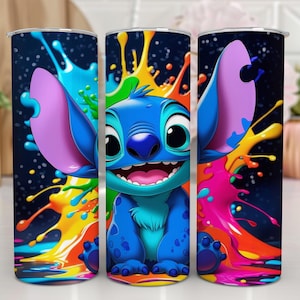 Puede incluir: Tres vasos de acero inoxidable con un personaje de dibujos animados azul, orejas grandes y una amplia sonrisa, rodeados de salpicaduras de pintura coloridas. El fondo es azul oscuro con motas blancas. Los vasos son cil&iacute;ndricos.