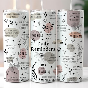 May include: Set of three white tumblers with black and pink floral designs and inspirational quotes. The quotes include "My inner strength is invincible", "I am powerful and fearless", "I believe in the woman I'm becoming".