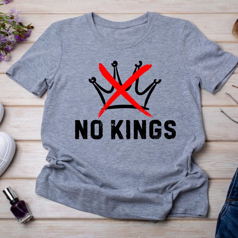 May include: A heather gray t-shirt with a black crown design crossed out in red, and the words "NO KINGS" in black block letters. The shirt is made of a soft material.