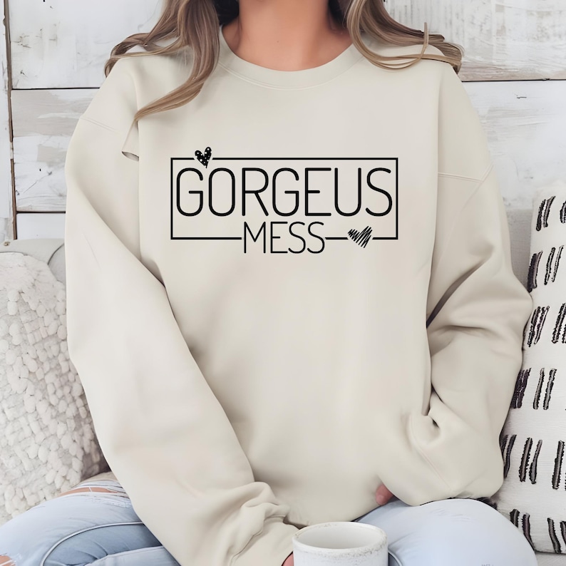 May include: A cream coloured sweatshirt with the text "GORGEOUS MESS" in a black rectangle with a small heart above and below the text.