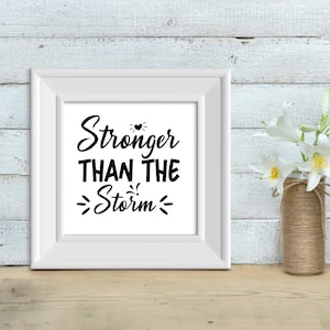 May include: White framed print with black text that reads "Stronger Than The Storm" with a small heart symbol above the word "Stronger".