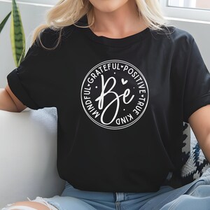 May include: Black t-shirt with a white circle graphic that says "Be" in a script font. The circle is surrounded by the words "Mindful, Grateful, Positive, True, Kind".