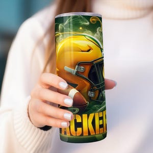 Pode incluir: Um copo verde e amarelo com um capacete de futebol e a palavra "Packers" nele.