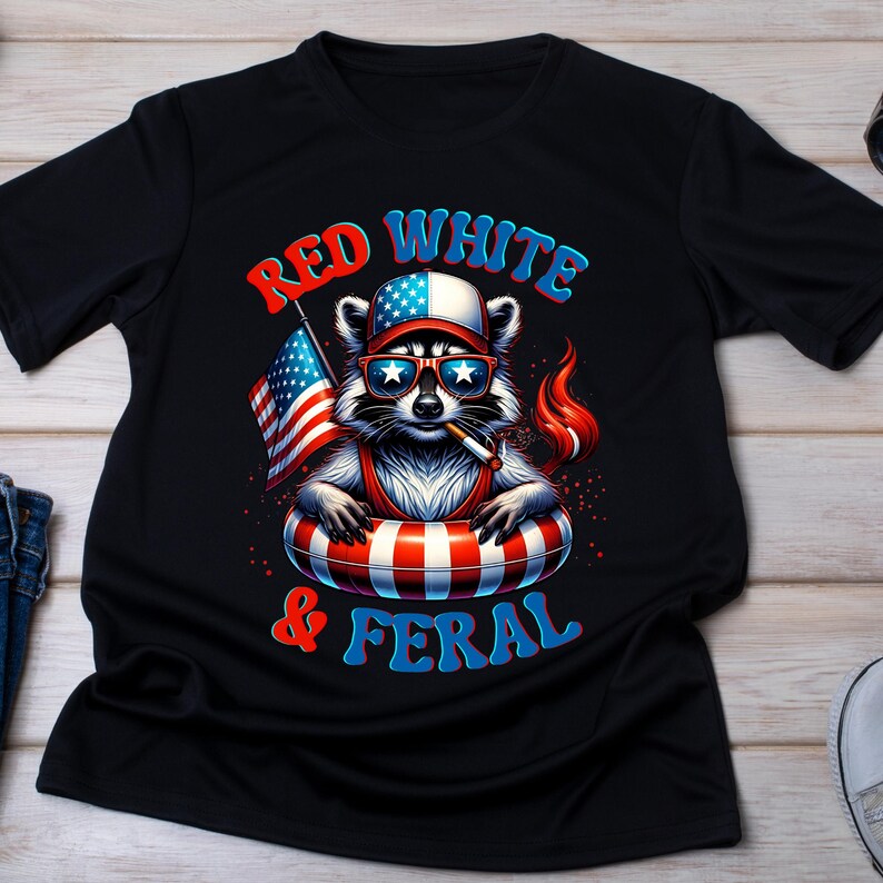 May include: Black t-shirt with a cartoon raccoon wearing sunglasses, a hat, and a life preserver, holding an American flag and a lit cigarette. The text reads "Red White & Feral" in red and blue.