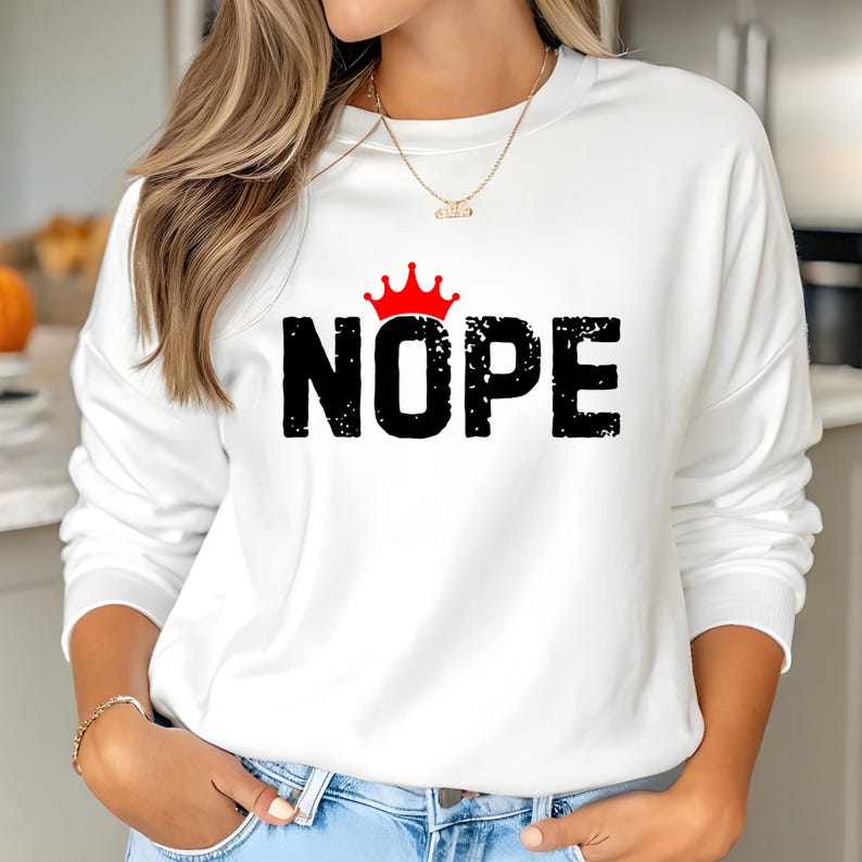May include: White sweatshirt with the word "NOPE" in black, distressed font, topped with a red crown graphic. The sweatshirt is a casual style, suitable for everyday wear.