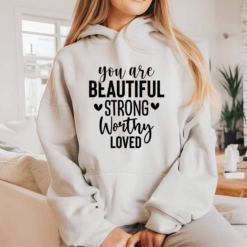 May include: A white hooded sweatshirt with black text that reads "You are beautiful strong worthy loved" with two small hearts on either side of the word "strong".