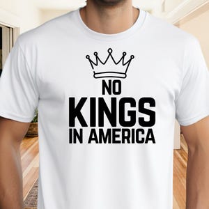 May include: White t-shirt with a black graphic design. The design features a crown above the words "NO KINGS IN AMERICA" in a bold, sans-serif font. The shirt is made of a soft material.