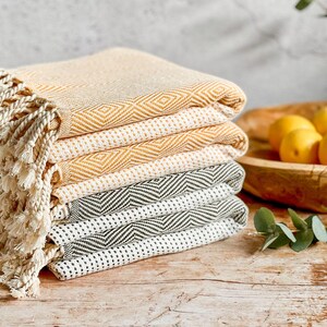 Peut inclure: Une pile de serviettes en coton tissées en jaune et gris avec des franges. Les serviettes sont pliées et empilées sur une surface en bois.