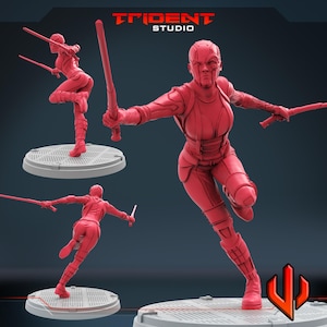 May include: A red figurine of a female warrior in a dynamic pose, holding two swords. The figure is on a circular platform, with the Trident Studio logo visible in the background. The warrior is wearing a form-fitting suit.