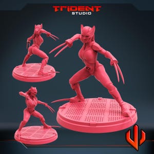 May include: Three pink figurines of a female superhero with claws, posed on circular platforms. The superhero is wearing a form-fitting suit and a mask with pointed ears. The Trident Studio logo is visible in the top left corner.