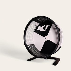 Puede incluir: Rueda de hámster negra y blanca con un logotipo de ardilla. La rueda tiene un diseño de tablero de ajedrez negro y blanco y una jaula de malla negra. La rueda está sobre un soporte negro con tres patas.