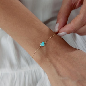 Peut inclure: Un bracelet en or délicat avec un charm en forme de cœur turquoise. Le bracelet est porté au poignet, mettant en valeur la fine chaîne et la couleur vive du pendentif en forme de cœur. Un bijou simple et élégant.