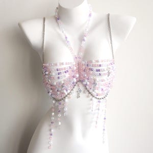 Può includere: Top di perline rosa, viola e bianco, esposto su un manichino. Il top presenta un collo all'americana e spalline a catena argentate. Fili di perline drappeggiate pendono dal basso e sono attaccati piccoli ciondoli argentati.