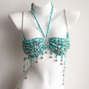 May include: A turquoise beaded top with silver chain straps and a matching necklace. The top features a central silver embellishment and dangling silver charms. The beads are a mix of turquoise and silver, creating a unique design.