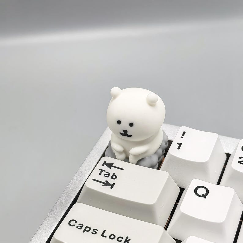 May include: A white keyboard with a small white bear figurine sitting on the Tab key. The bear has black eyes and a small black nose.