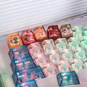 Op de afbeelding: Een wit toetsenbord met transparante toetsen en gekleurde toetsen met ingebedde afbeeldingen. De toetsen hebben de letters QWERTY en de woorden Tab, Caps Lock en Shift.