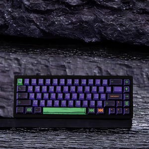 May include: A black mechanical keyboard with purple and green keycaps. The keyboard has a green and black spacebar and a green and black escape key. The keyboard also has a row of orange keys with a green and black border. The keyboard is sitting on a black surface.