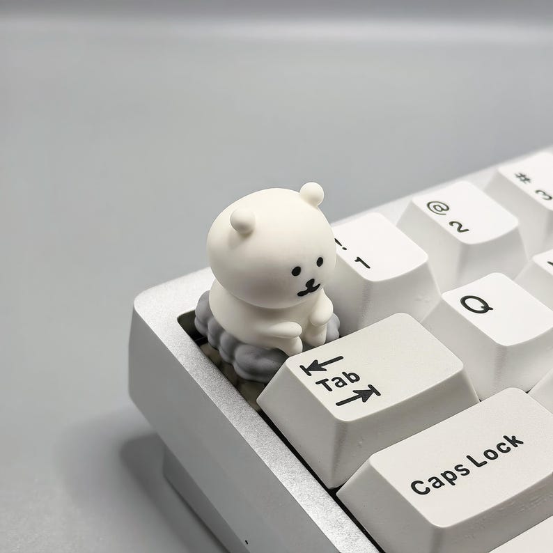 May include: A white keyboard with a small white bear figurine sitting on the Tab key. The bear is sitting on a cloud-shaped base.
