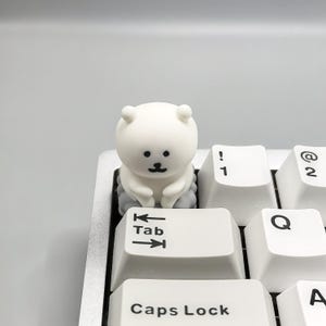 May include: A white keyboard with a small white bear figurine sitting on the "Tab" key. The bear is sitting on a small gray cloud.