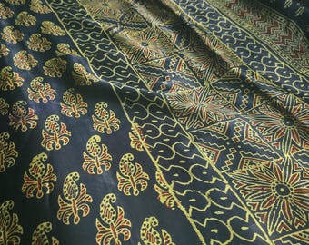 May include: A dark fabric featuring a repeating pattern of yellow and red paisley motifs alongside vertical bands of geometric shapes, including star-like designs and zigzag lines, printed across the surface of the textile material.