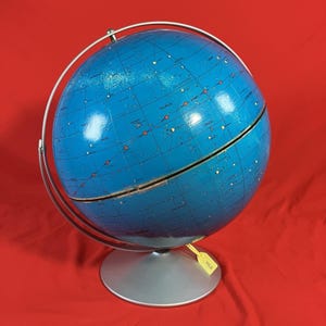 May include: A vintage blue celestial globe with constellations and star names. The globe is mounted on a silver-colored base with a metal meridian ring. The globe has a yellow tag attached.