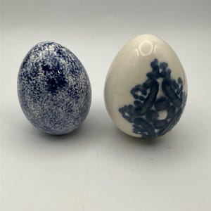 Peut inclure: Deux objets décoratifs en forme d'œuf. Un œuf présente un motif tacheté bleu foncé dense sur une base blanche. Le second œuf est blanc uni avec un motif floral bleu foncé peint au centre de la surface avant.